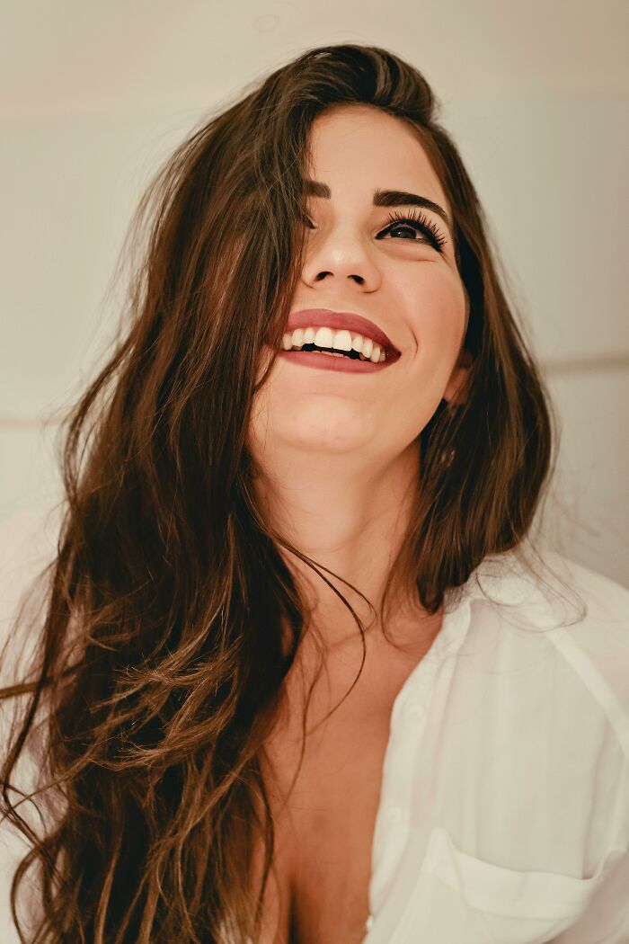 Woman smiling confidently, wearing a white shirt, showcasing beauty that confuses men.