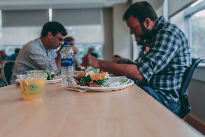 Adults eating sandwiches at a cafeteria table, showcasing a calm meal setting.