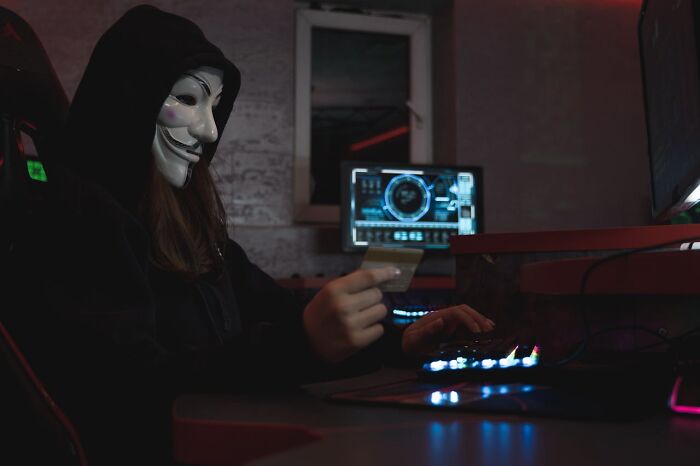 Person in a hoodie and mask using a computer, reflecting hidden aspects of a profession.