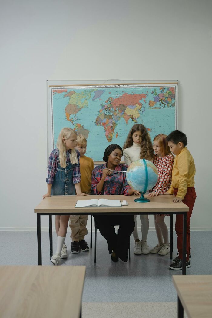 Teacher discussing geography with children, pointing to a globe in front of a world map.