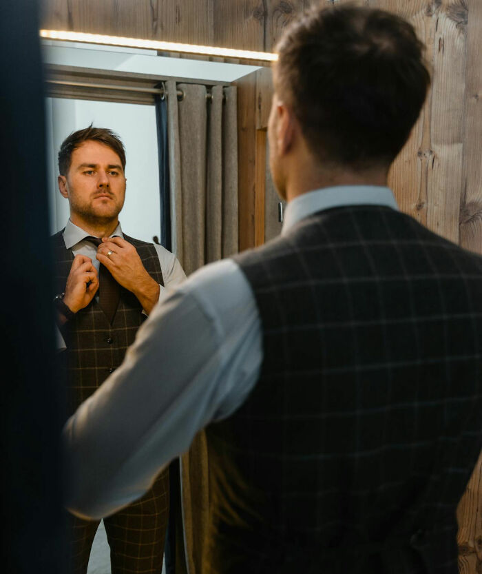 Man adjusting tie in mirror, reflecting a moment of self-awareness and obvious things just becoming clear.