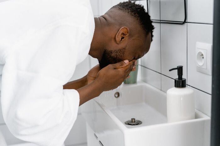 Man practicing hygiene by washing face in a bathroom sink.
