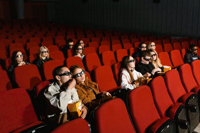 Audience wearing 3D glasses eating popcorn in a theater, illustrating rising restaurant food prices and changing consumer habits.