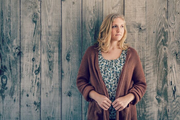 A woman stands against a wooden wall, contemplating life abroad.