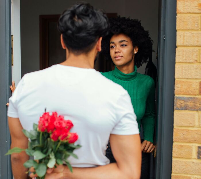 Man hiding red roses behind his back, talking to woman at the door, exploring why guys slept with a married woman.
