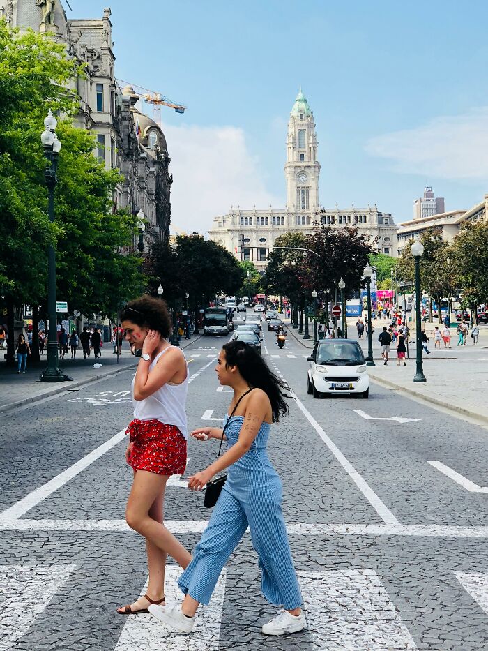 Two women crossing a street abroad with a historic building in the background, capturing the experience of Americans abroad.