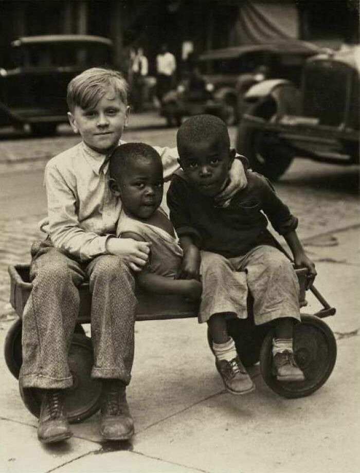 Three children sitting together on a small cart in a vintage photo showing history up close and childhood moments.