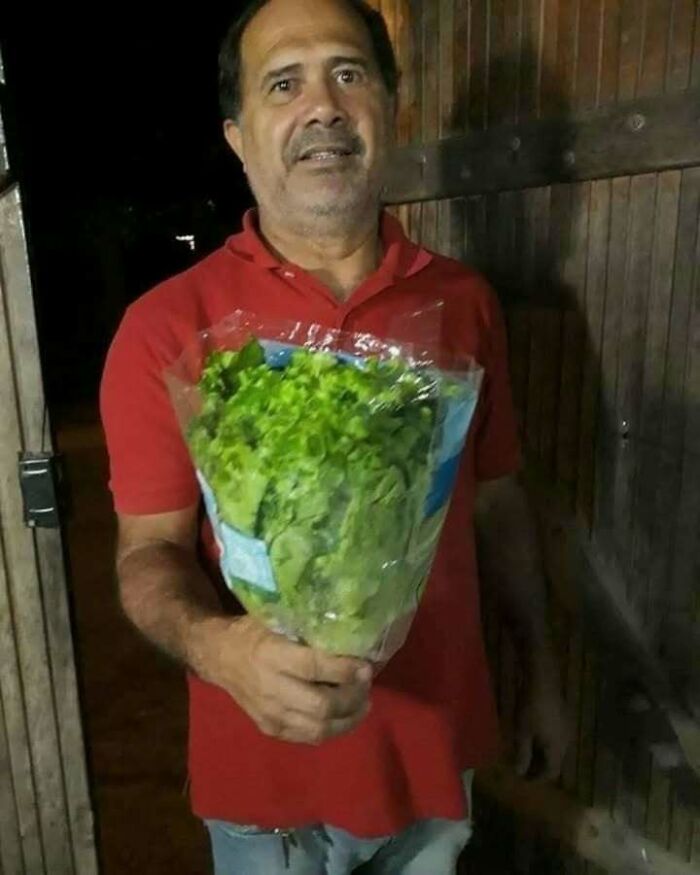 Man holding a lettuce bouquet, wearing a red shirt and smiling humorously. Perfect for sharing funny memes with friends.