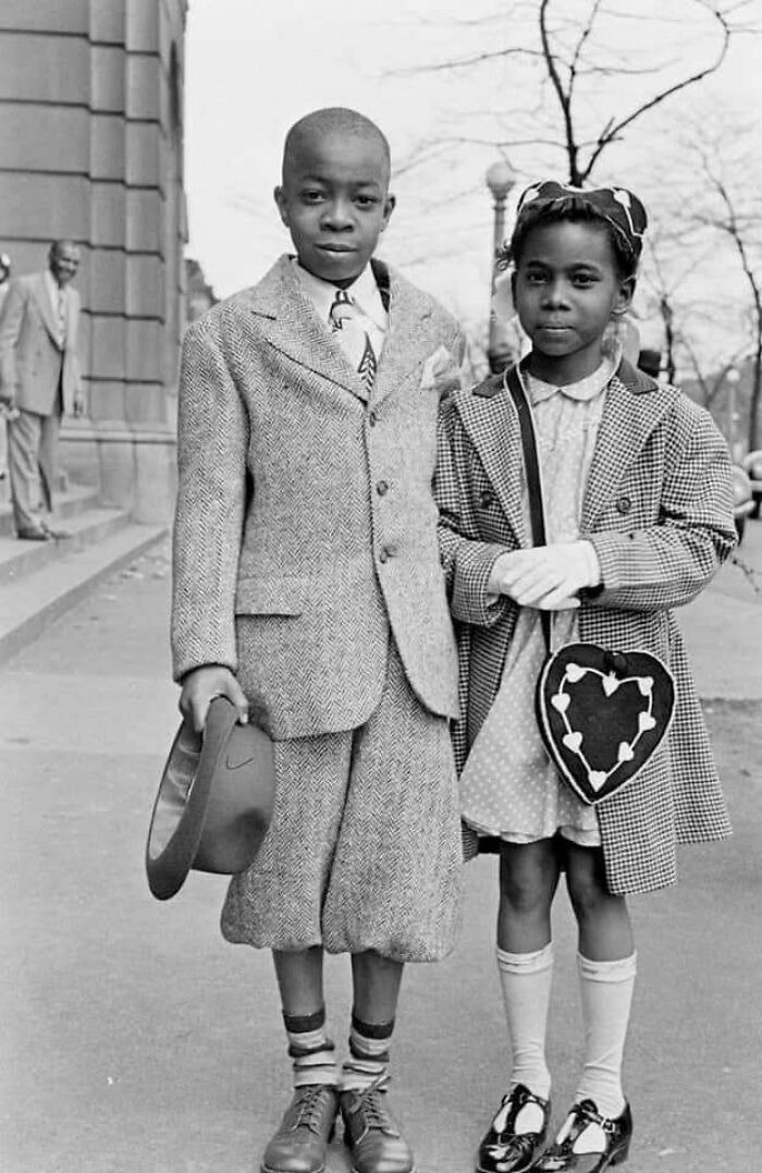 Vintage photo of two children dressed in period clothing, capturing history up close on a city sidewalk.