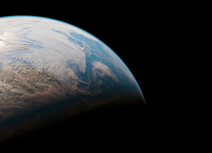View of Earth from space under sunlight, showcasing clouds over continents.