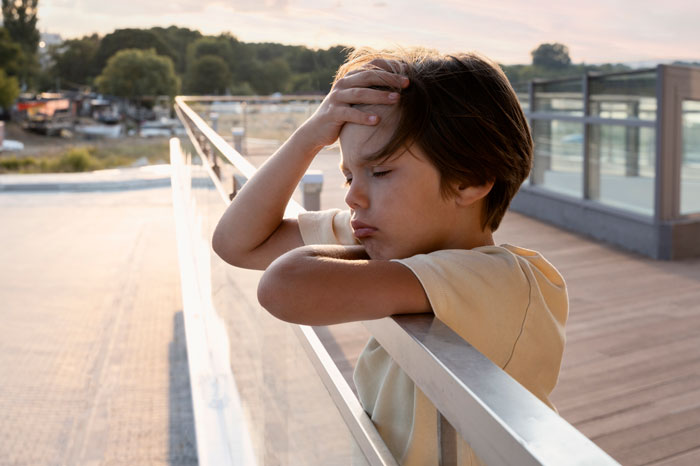 Upset child in the sun, leaning on a railing, representing concerns about lack of hydration.