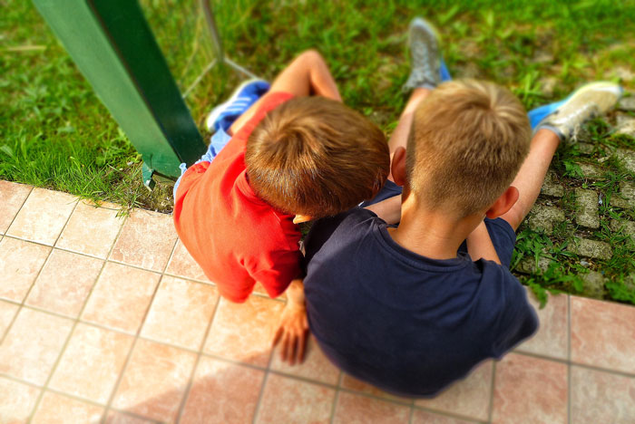 Kids sitting on grass under the sun, with no visible water or bathroom nearby.