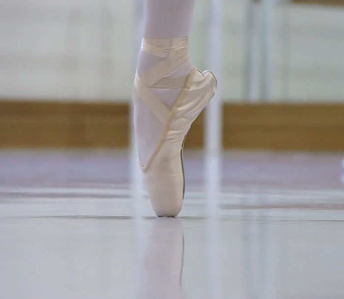 Ballet dancer's pointe shoe on studio floor, emphasizing dance grace and skill.