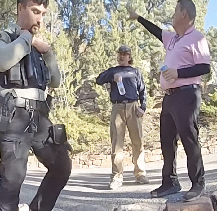 Police and two men discussing outside, referencing Gene Hackman's dog related incident in a wooded area.