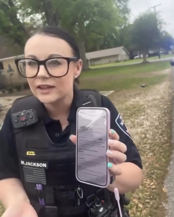 Police officer showing a phone screen during a street incident involving walking on the wrong side of the road.