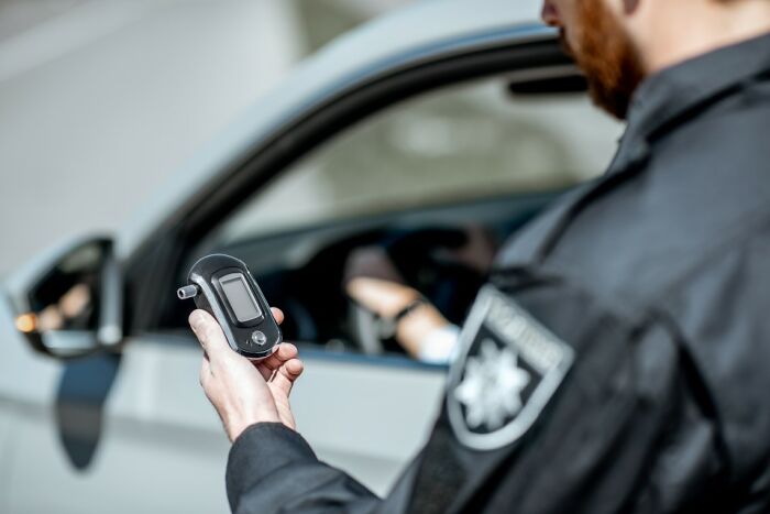 Police officer holding a breathalyzer while standing beside a car.