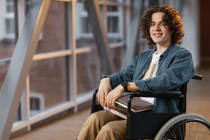 Smiling person in a wheelchair holding books, reflecting on life after an accident.