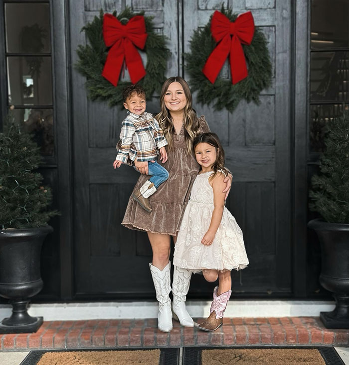 Woman with two children, holiday wreaths on door, memorializing TikTok star 'Okay Baby' in heartfelt setting.