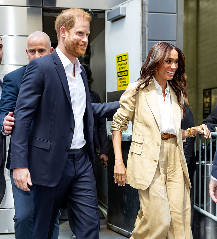 Meghan Markle and a man in formal attire walking outside a building with a security guard.