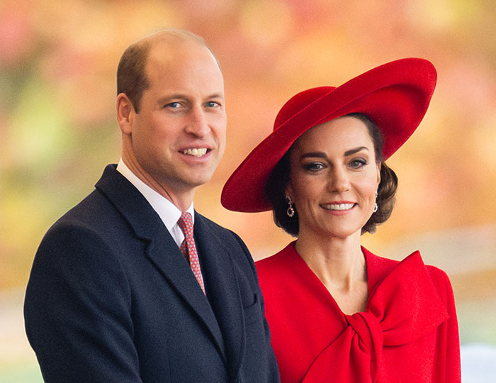 Prince William with companion in formal attire at a public event, against a colorful background.