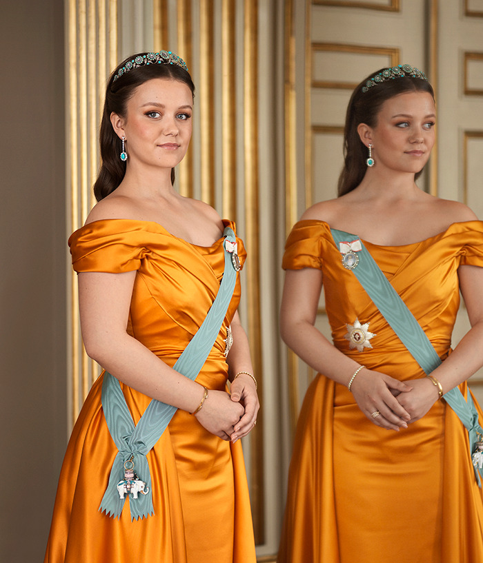 Royal princess in orange gown, wearing a tiara, reflects in a mirror, holding an iPhone in an elegant setting.
