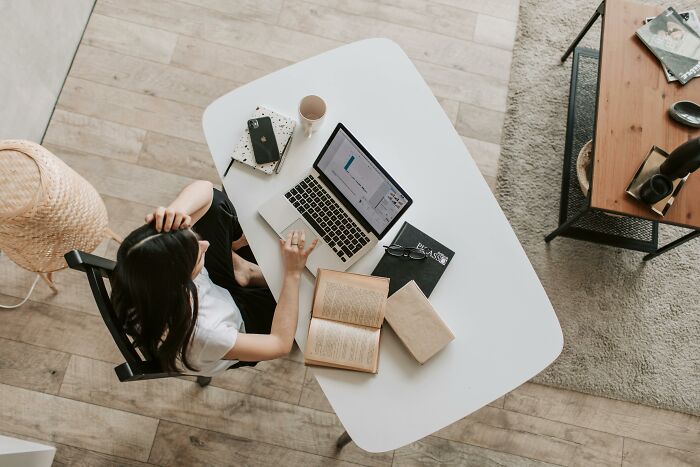 Person at a desk with a laptop and books, pondering productivity tips, in a home office setting.