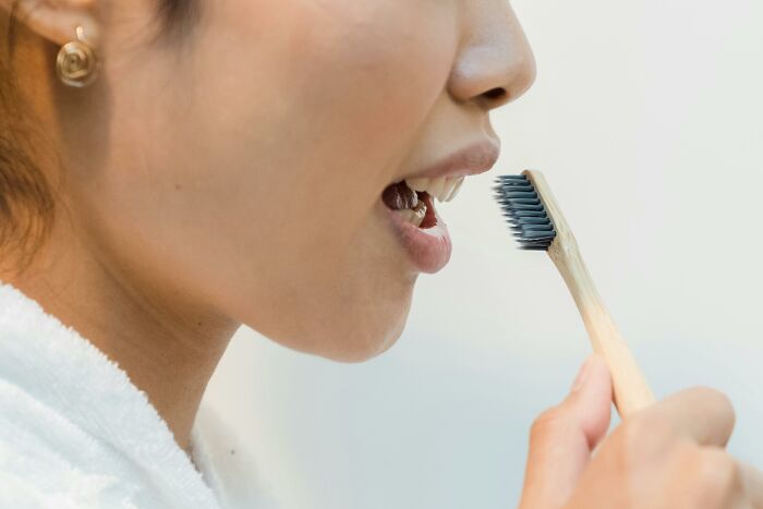 Woman brushing teeth with bamboo toothbrush, emphasizing hygiene instead of productivity tips.