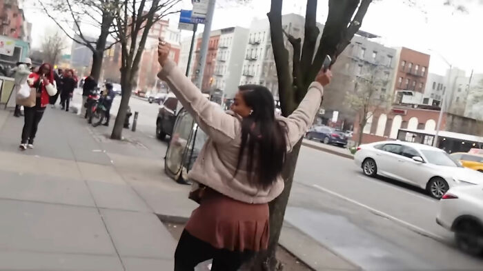 A woman gestures on a city sidewalk during an abortion street interview, with cars and buildings in the background.