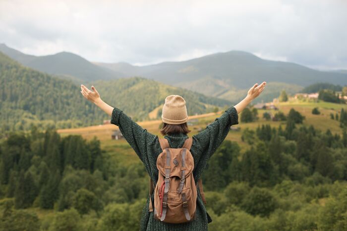 Person in a hat and backpack embracing nature, symbolizing quality of life improvement in a serene mountain landscape.