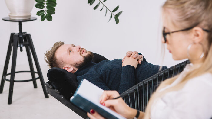 Person lying on a couch during a therapy session, discussing quality of life improvement with a therapist taking notes.