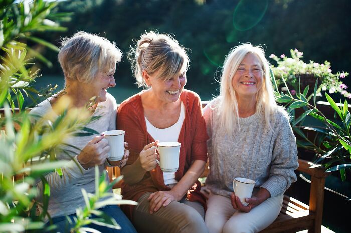Elderly women enjoying coffee together on a sunny patio, highlighting quality of life improvement through social interaction.