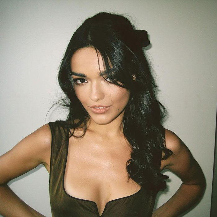 I don&rsquo;t know who this person is, but they are posing confidently with long dark hair against a neutral background.