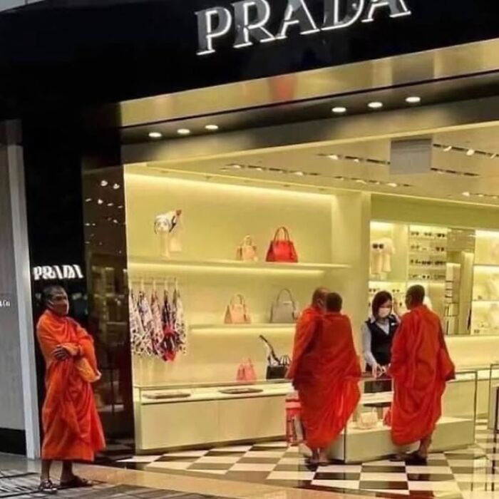 Monks in traditional robes stand by a Prada store, creating a humorous contrast.