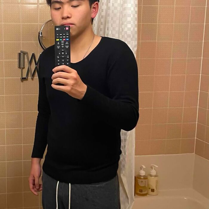 Person humorously posing with a TV remote in a bathroom mirror selfie.