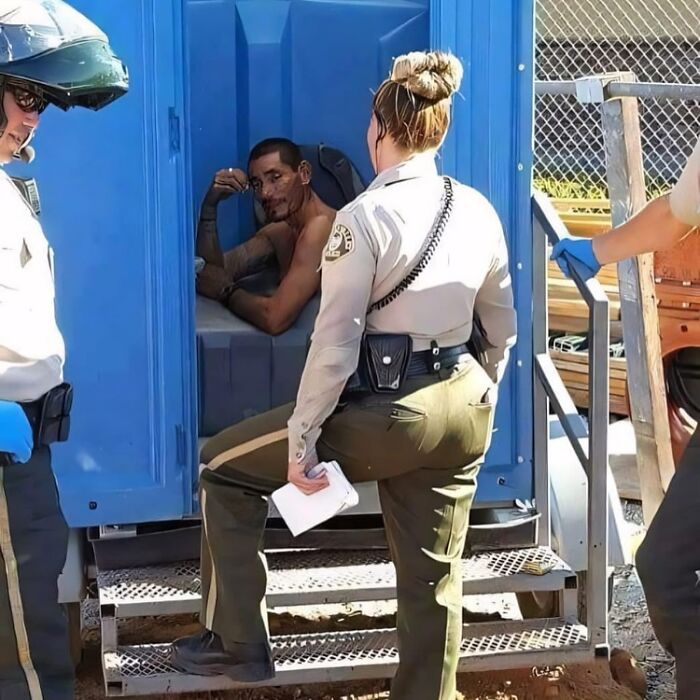 Police officers interacting with a man inside a portable toilet.