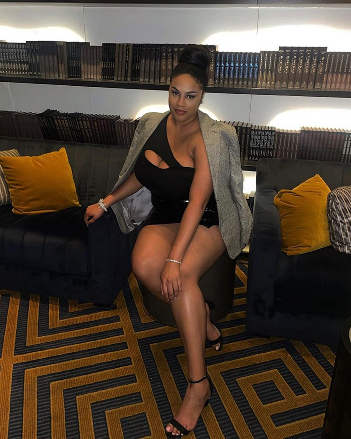 Woman seated stylishly in a lounge, wearing a black dress and blazer, related to stranger braided hair story.