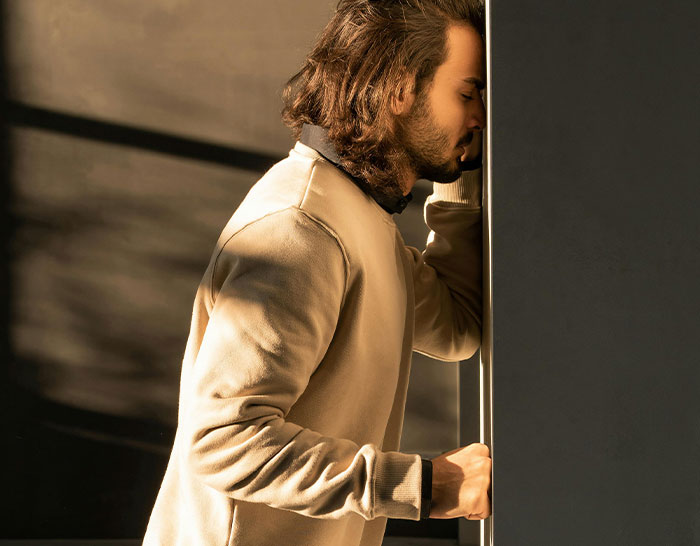 Man leaning against a wall, appearing contemplative, capturing the stress often felt during a recession.