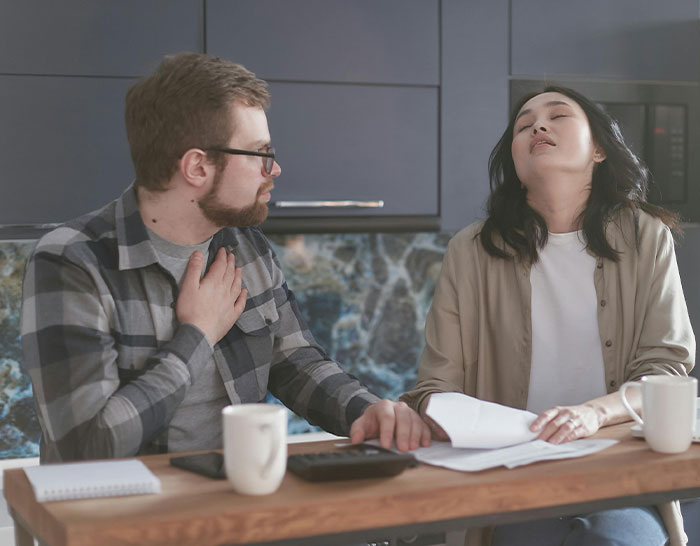 Two people at a table, visibly stressed, discussing recession impacts with papers and coffee mugs.