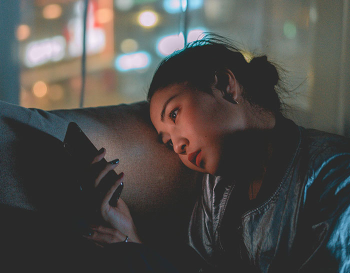 Person in a dimly lit room, reflecting on a recession while looking at their phone.