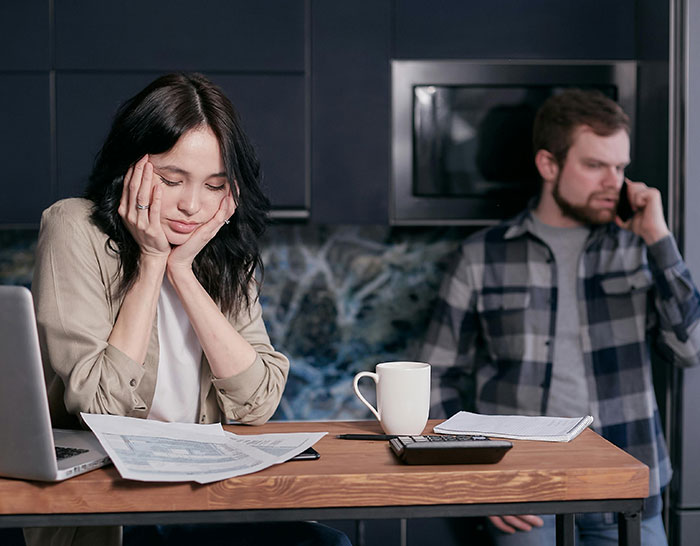 Woman appearing stressed over finances during a recession, with a man on phone in the background.