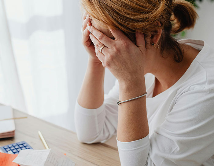 Woman at desk looking stressed about recession finances, covering face with hands.