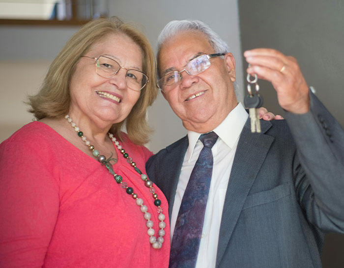 Senior couple smiling, holding keys, related to recession experiences.