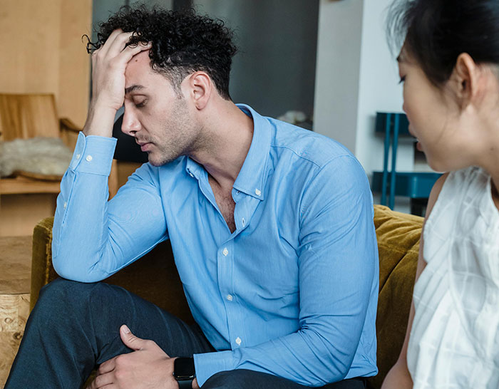 Man in blue shirt appearing stressed, sitting beside a woman, illustrating recession experience challenges.