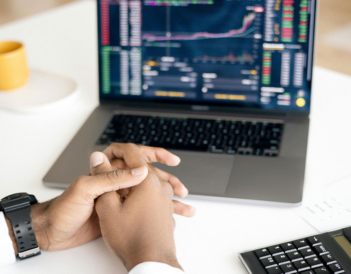 Person analyzing recession data on a laptop, hands clasped in thought, with a focus on market trends and graphs.