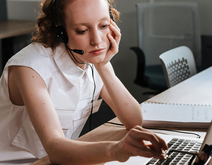 Person in a headset looking concerned while working on a laptop, illustrating recession impact.