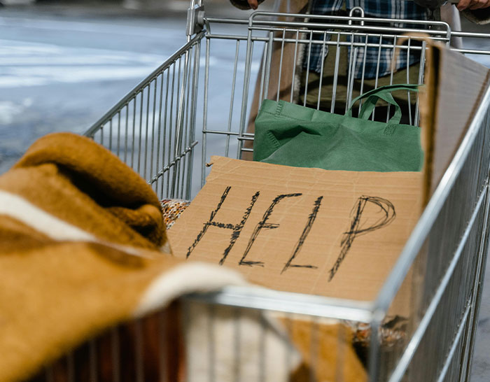 Shopping cart with a cardboard "HELP" sign, highlighting recession impact.