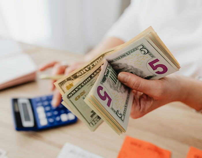 "Person counting cash with a calculator, symbolizing recession impact on personal finances."