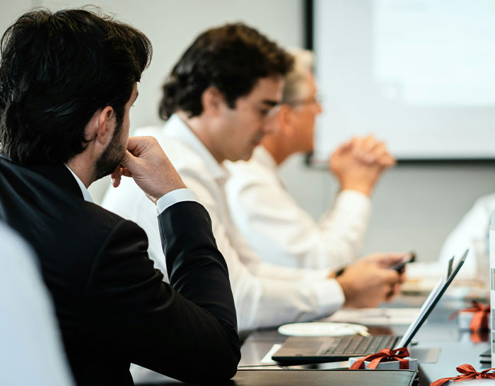 People in a business meeting, discussing recession impacts around a conference table with laptops and notes.