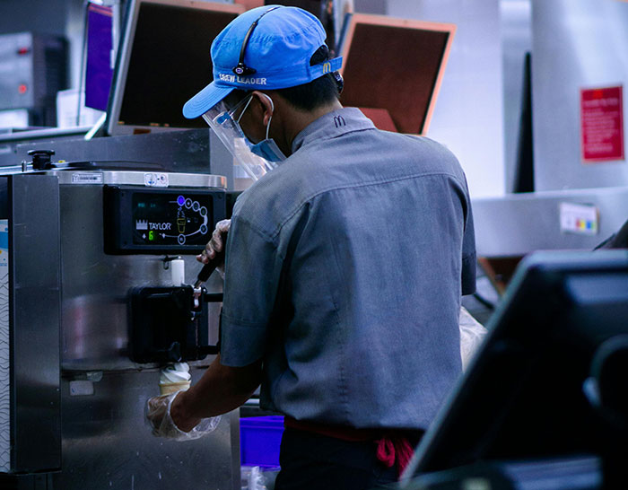 Fast food worker in uniform and mask serving ice cream during a recession.