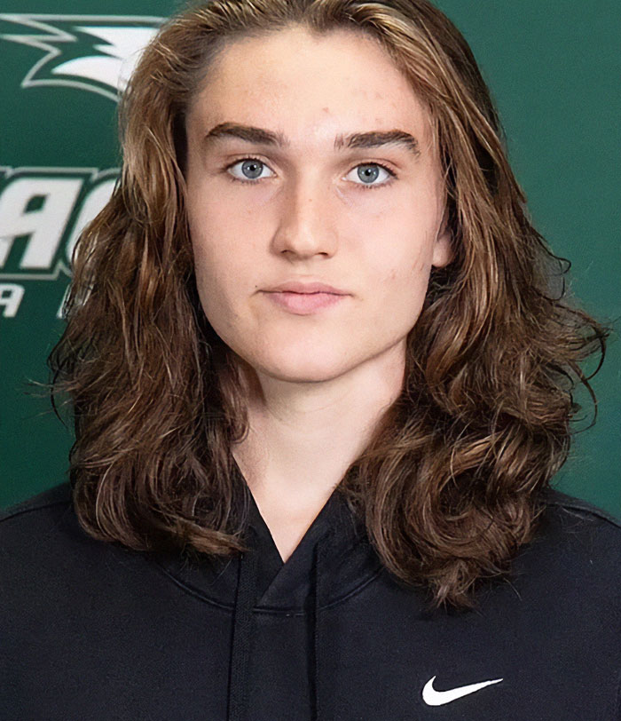 Trans athlete in controversy, wearing a black hoodie, standing against a green backdrop.